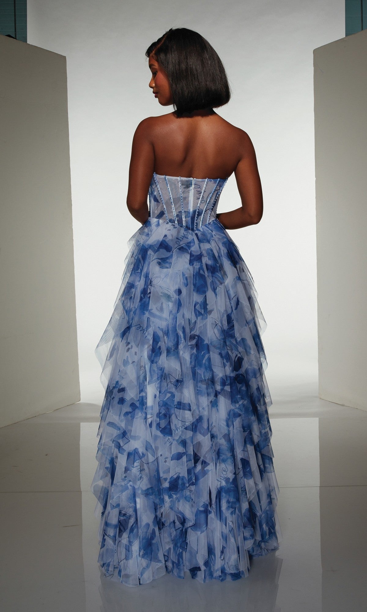 A woman with a bob haircut is shown from the back wearing the Alyce 62041 long prom dress, featuring a strapless floral print, tiered ruffled skirt, and structured corset bodice.